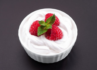 whipped cream bowl with raspberries and  mint leaves  topping close-up on gray background
