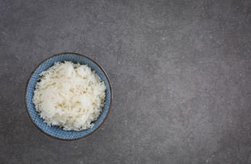A blue ceramic bowl with white jasmine rice. Overhead shot. Dark gray background 
