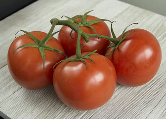 four red tomatoes on vine on wood table