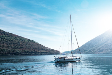 Fototapeta na wymiar Sailing yacht swimming at blue sea near forest mountains