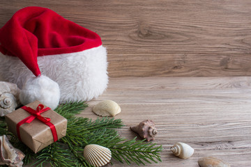 Obraz na płótnie Canvas Gift boxes and Santa hat and seashells on Christmas tree. Wood b