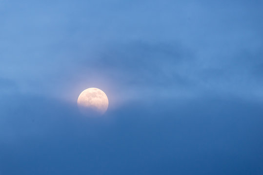 A full moon rises behind a bank of blue clouds