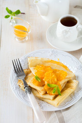 Thin crepes with orange citrus sauce for breakfast on light background. Selective focus.