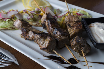 Pork sticks with white sauce and fresh salad in white plate.