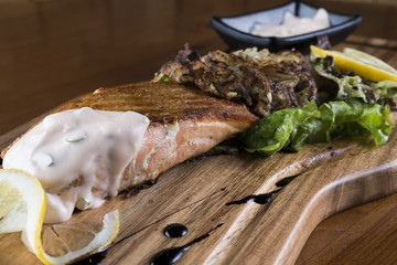 Salmon filet with baked onion, green salad, limes and fresh sauce on a wooden platter.