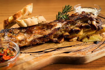 Pork ribs with potatoes and bread loafs on a wooden platter