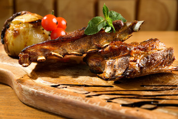 Pork ribs with barbecued onion and cherry tomatoes on a wooden platter