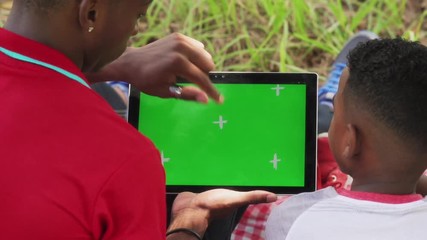 Happy black people in city park. African american family with young man and child using computer for internet and email. Leisure for man and boy with ipad tablet with green screen