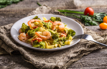 Pasta linguine with shrimps and broccoli in plate on wooden background.