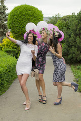 Fototapeta premium Summer outdoor portrait of three friends fun girls taking photos with a smartphone at bright sunset