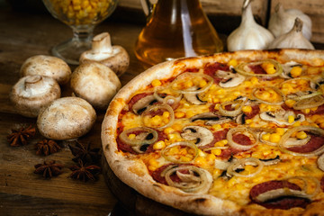 Whole pizza with sausages, corn and onion on wood table with ingredients