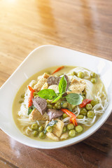Green curry chicken with thai rice noodles in ceramic plate on wood table with sunlight background, Thai Food.