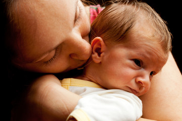 Young mother holding her baby boy. Isolated on black background