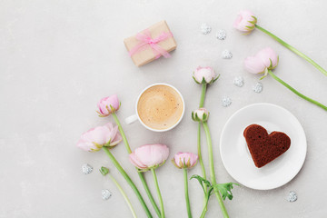 Obraz na płótnie Canvas Breakfast for Valentines day with cup of coffee, gift, flowers and cake in shape of heart on gray table from above in flatlay style.