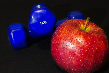 red apple with blue dumbbells on a black background. Shallow depth of field