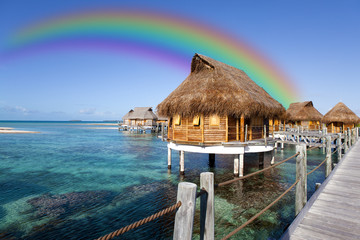 huts over the sea and a rainbow over them