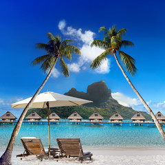 two beach chairs and solar umbrella under a palm tree and a view of the sea and mountains. Tahiti