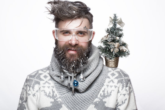Funny bearded man in a New Year's image with snow and decorations on his beard. Feast of Christmas. Photos shot in the studio.