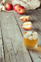 glass of juice with ice and apple in background