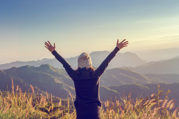 Carefree Happy Woman Enjoying Nature on grass meadow on top of mountain cliff with sunrise. Beauty...