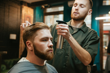Hipster man getting haircut by hairdresser while sitting in chair.