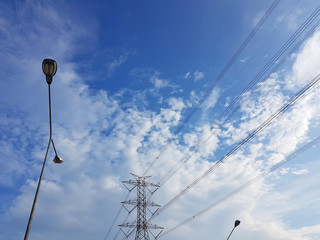 High-voltage tower in cloudy blue sky background with street light