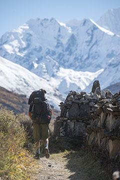 Hiking past a traditional Mani stone wall in the Langtang Valley with views of Ganchempo in the distance, Langtang Region, Himalayas, Nepal