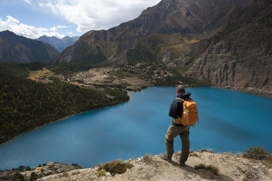A trekker looks out at the turquoise blue Phoksundo Lake, Dolpa Region, Himalayas, Nepal