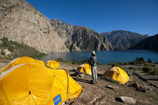 A trekker looks out at the turquoise blue Phoksundo Lake, Dolpa Region, Nepal