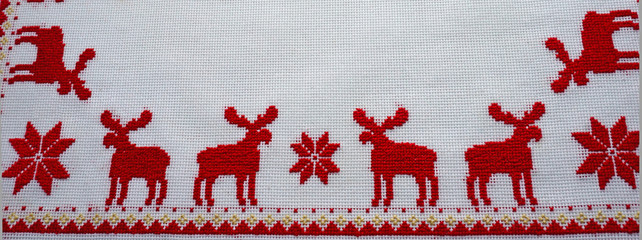 Cross-Stitched red deer on the white tablecloth. Christmas background
