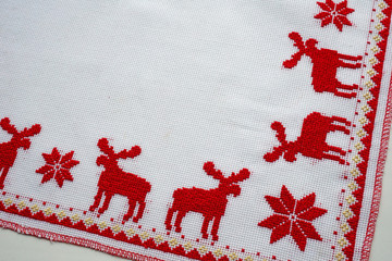 Cross-Stitched red deer on the white tablecloth. Christmas background
