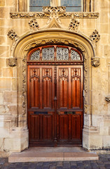 Fototapeta na wymiar Heavy closed wooden double door at an old church. Above the arch are chiseled floral ornaments, the door frame has a rounded top, wooden decorative carvings. Around it is a stone wall with blocks.