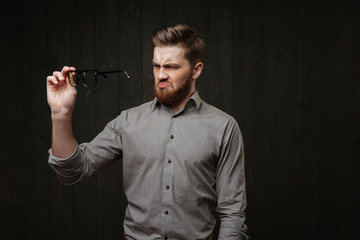 Portrait of an unsatisfied man in shirt looking at eyeglasses