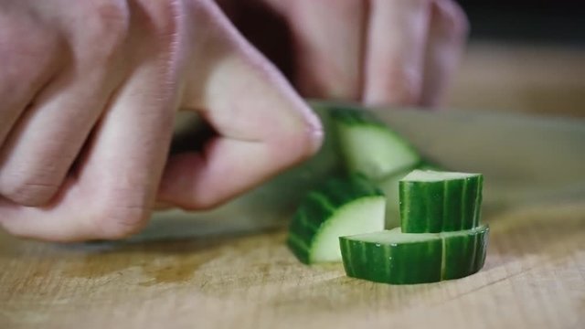Closeup of male hands cutting fresh cucumber on wooden board and then putting pieces together