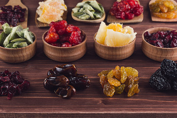 Assortment of dried fruits closeup on brown wooden background. Decorative border of dry exotic fruit in spoons, bowl.
