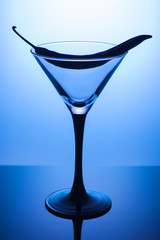Empty cocktail glass martini with red hot chili pepper on a blue background. Transparent glass, vertical photo.