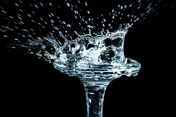 Close-up a drop of water is split on the glass in the form of a crown isolated on a black background