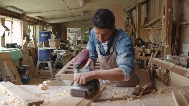 PAN of concentrated male carpenter using grinder machine and smoothing wood plank