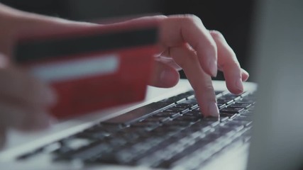 Online shopping. Female hand holding a red credit card and shopping online. Woman using computer for on line purchase with credit card and typing on a black keyboard