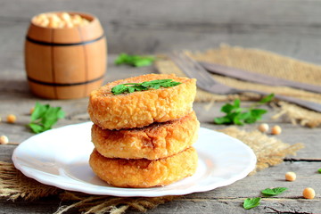 Delicious pea burgers on a plate. Fried vegetarian burgers made from dried peas and decorated with fresh herbs. Decorative wooden barrel, cutlery on a wooden table. Vegetarian meal recipe. Closeup