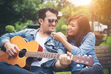 Fototapeta na wymiar Young couple in love playing acoustic guitar in the park while s
