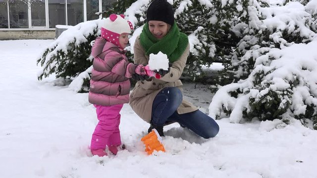 Playful mother with excited daughter girl build snow castle and destroy it