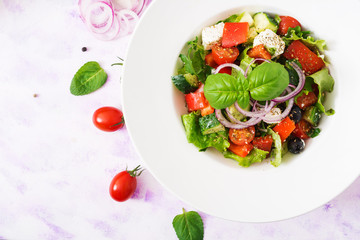 Greek salad with fresh tomato, cucumber, red onion, basil, lettuce, feta cheese, black olives and Italian herbs. Top view