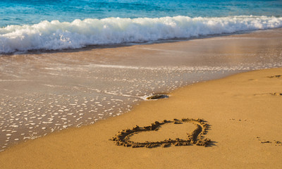 Drawing a heart on the beach sand on the beach with sea waves in the background. Selective focus. Beautiful deserted beach.