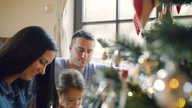 Young family with daugter at Christmas tree at home.