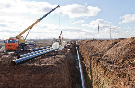 Construction work on the pipe laying of the pipeline into the trench using a crane