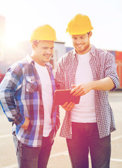 smiling builders in hardhats with tablet pc