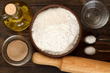Ingredients for pizza dough on dark wooden background.