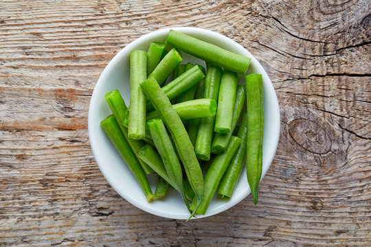 Bowl of green beans on wooden table, from above
