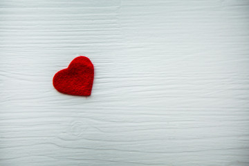 Fototapeta na wymiar Маленькое красное сердце из фетра на белом деревянном столе.